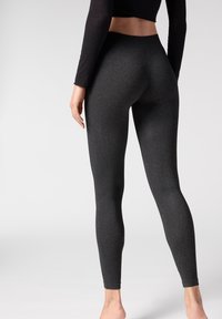 Schwarze hochtaillierte Leggings mit glatter Textur, figurbetonter Passform und dezentem meliertem Muster, die bis zu den Knöcheln reichen.