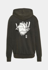 Sweat à capuche vert foncé avec un graphisme blanc d'un bras fléchi et des points d'exclamation stylisés dans le dos.