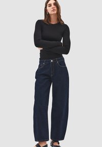 Top nero a maniche lunghe abbinato a jeans in denim blu scuro a gamba larga con vita alta, rivetti e dettagli di cucitura a contrasto.