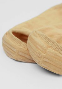 Beige strikkede usynlige sokker med skridsikre silikone striber på hæle og såler, liggende fladt på en hvid overflade.