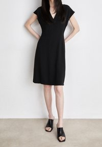 Svart kortärmad klänning med V-ringning, tillverkad av ett mjukt tyg. Designen är figurnära vid bysten och vidgar sig mjukt vid fållen.