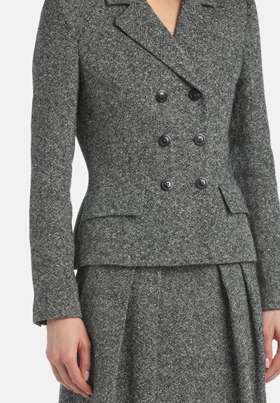 Blazer en tweed gris avec une fermeture à double boutonnage, un col cranté et des poches latérales, associé à une jupe plissée assortie.