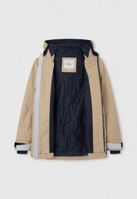 Tann vandtæt jakke med marineblå indvendig, lynlås-lukning, elastiske manchetter og reflekterende detaljer på ærmerne. Designet til varme og komfort.