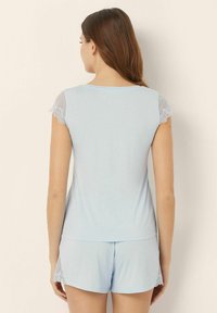 Set de somn de culoare albastru deschis, format dintr-o bluză cu mânecă scurtă, cu accente din dantelă, și șorturi asortate. Material moale cu o croială lejeră.