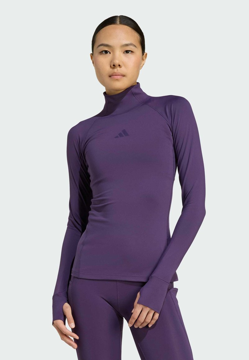 Haut de sport violet à manches longues avec un col montant, texture lisse, orifices pour les pouces et embellissement logo discret sur la poitrine. Design ajusté.