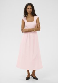 Rosa Maxikleid mit quadratischem Ausschnitt und ärmellos, mit engem Oberteil und geraffter Taille, aus glattem Stoff. Schwarze Pumps mit Absatz.