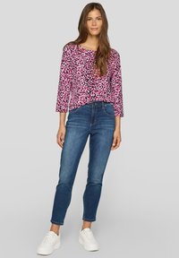 Long-sleeve top in pink with black and white leopard print, paired with denim jeans. White sneakers complete the casual outfit.