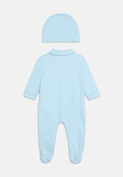 Body bébé bleu clair à manches longues avec pieds et bonnet assorti bleu clair, posé à plat sur fond blanc.