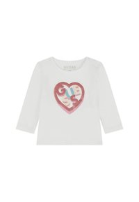 Maglietta bianca a maniche lunghe con un grafico di un cuore di glitter rosa che presenta il testo "GUESS" in blu, giallo e rosso. Realizzata in cotone biologico.