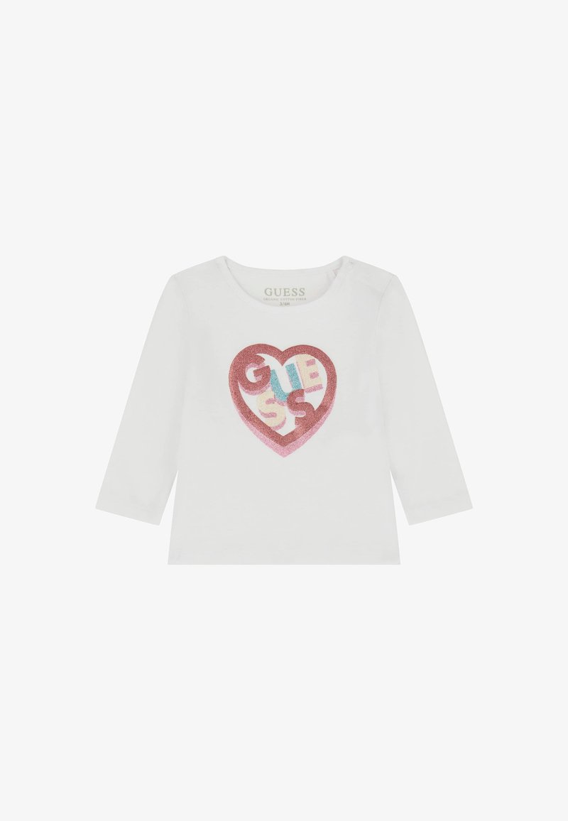 Maglietta bianca a maniche lunghe con un grafico di un cuore di glitter rosa che presenta il testo "GUESS" in blu, giallo e rosso. Realizzata in cotone biologico.