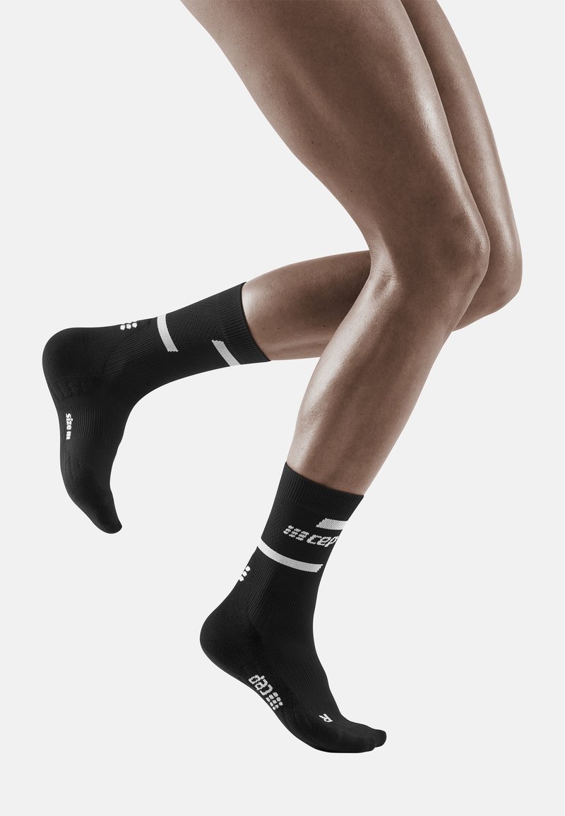 Schwarze Sportsocken mit weißen Akzenten und Logos, enganpassendes Design, knielange Länge, aus strukturiertem Material, konturiert für Komfort.