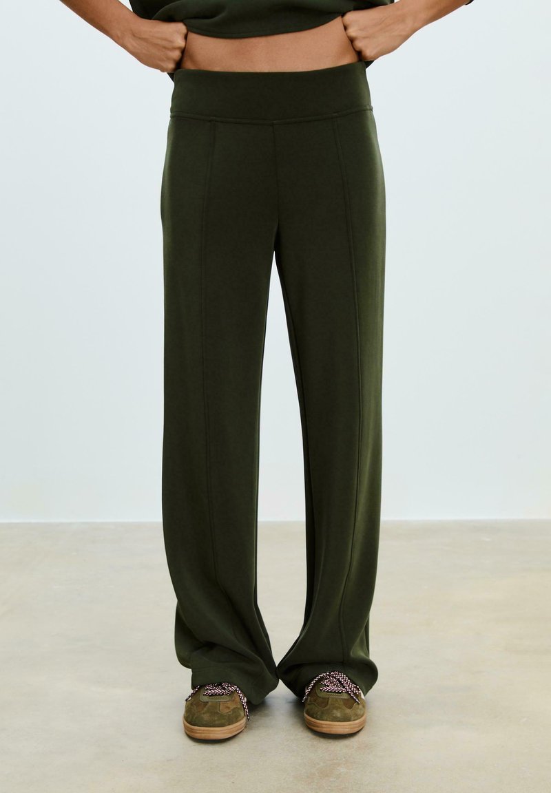 Pantaloni a gamba larga verde oliva con una vita alta e liscia e cuciture verticali. Abbinati a scarpe in suede verdi con lacci a fantasia.