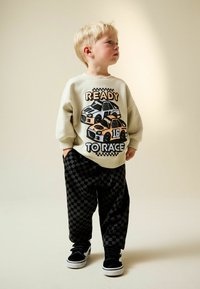 Bluză gri deschis cu grafica „READY TO RACE” și ilustrații cu mașini; asortată cu pantaloni negri cu carouri și adidași negri.