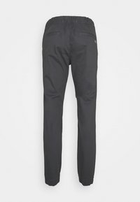 Pantalon slim gris foncé avec taille et poignets élastiques, présentant deux poches passepoilées au dos sur un fond uni.