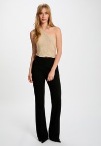 Top beige metallizzato a spalle scoperte con texture perforata abbinato a pantaloni neri a vita alta e svasati. Entrambi i capi presentano linee pulite.