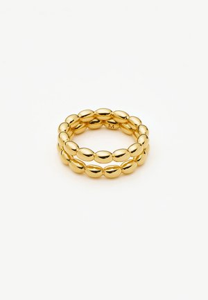 Zelta toņa dubultais gredzens no gludiem, ovālas formas pērlīšu saišķiem, attēlots uz vienkārša balta fona.