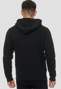 Sudadera negra hecha de una tela suave, con un bolsillo tipo canguro, puños acanalados y capucha con cordón. Textura lisa con un corte relajado.