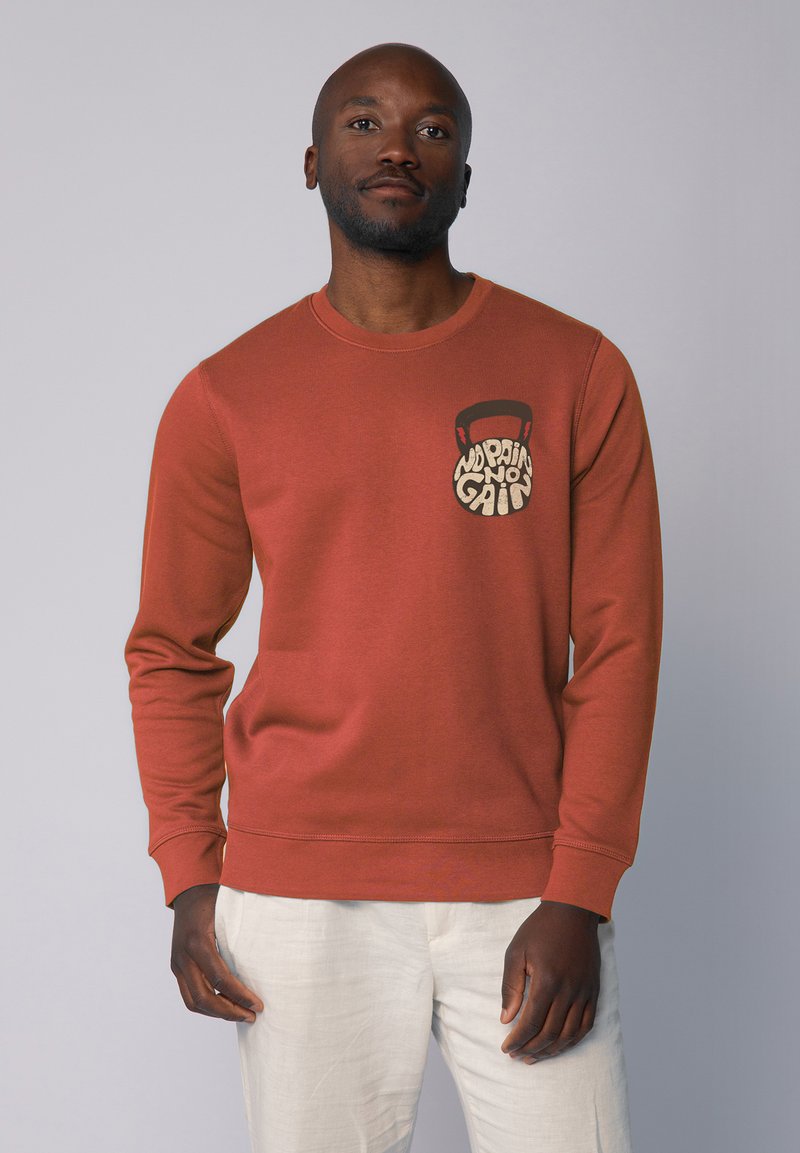 Rostfarbenes Sweatshirt mit Rundhalsausschnitt und einer Brusttasche. Glatte Textur, gerippte Bündchen und Saum.