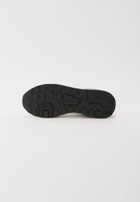 Svart gummisåle på en sneaker med mønster og merkevarenavnet "FILA" preget i midten.