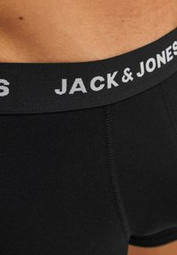 Schwarze Boxershorts aus glattem Stoff mit einem dicken schwarzen Gummibund, auf dem "JACK & JONES" in weißer Schrift steht, und eng anliegendem Schnitt.