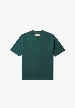 Zeleni pamučni majica s kratkim rukavima, okruglim izrezom i oznakom na lijevom rukavu. Tkanina izgleda glatko i ravnomjerno obojena.