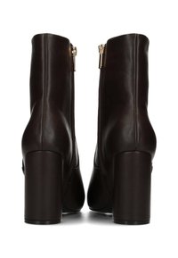 Botas de cuero marrón hasta el tobillo con un alto tacón cuadrado, que presentan cremalleras laterales y una textura suave. Diseño sencillo sin patrones visibles.