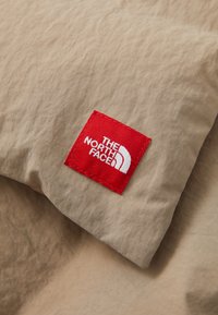Beige fabric with a textured surface and stitched red label featuring the white logo of The North Face in a corner.