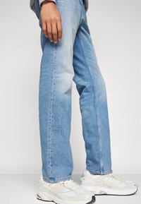 Lyseblå denimjeans med rett benpassform, med falmede områder og synlige sømmer. Kombinert med hvite treningssko.