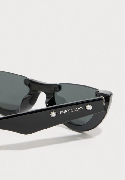 Čierne slnečné okuliare s tmavými sklami a elegantným tvarom mačacích očí. Obsahujú logo "JIMMY CHOO" a dva perlové akcenty na spánkoch.
