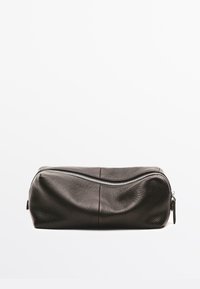 Borsa da toilette in pelle nera testurizzata con cerniera curva argentata, mostrata chiusa su uno sfondo bianco semplice.