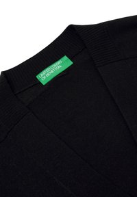 Cardigan nero realizzato in morbido tessuto a maglia, con un design a scollo a V. Include un'etichetta verde con la scritta "UNITED COLORS OF BENETTON" in bianco.