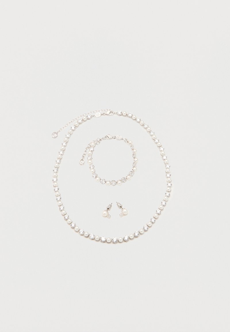 Κολιέ, βραχιόλι και σκουλαρίκια με εναλλασσόμενα λευκά μαργαριτάρια και διακριτικά στρογγυλά κρύσταλλα σε ασημένια αλυσίδα, τοποθετημένα πάνω σε ανοιχτό φόντο.