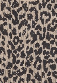 Stickad tyg med en krämfärgad bas och ett djärvt svart leopardmönster. Texturerad design med varierande former och storlekar av fläckar genom hela tyget.