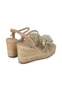 Sandali con zeppa beige con suola in espadrillas, caratterizzati da un accento di fiore in tessuto testurizzato e multiple cinghie incrociate.