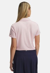 Ljusrosa pikétröja med klassisk krage, korta ärmar och Under Armour-logotyp på vänster ärm. Matchas med en marinblå plisserad kjol.