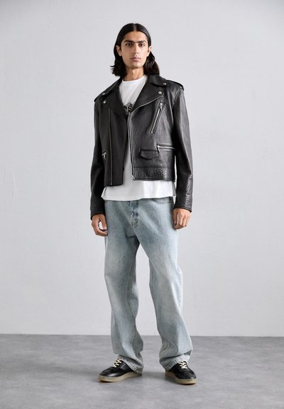 Black leather motorcycle jacket with silver zippers, paired with a white t-shirt and light blue loose denim jeans. Black sneakers complete the outfit.
