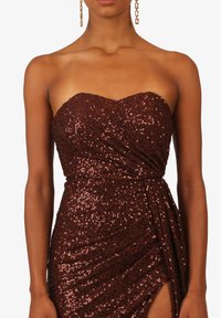 Vestito senza spalline di un profondo borgogna, ricoperto di paillettes con un design avvolgente, dotato di uno spacco alto e una texture liscia, completato da orecchini pendenti.