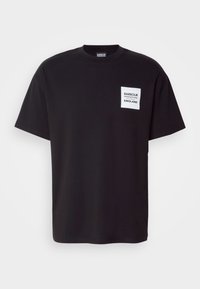 Černé bavlněné tričko s krátkým rukávem, s bílou etiketu na levé straně hrudi s nápisy "BARBOUR" a "ENGLAND".
