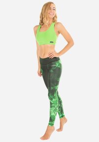 Groene sportbeha en zwarte leggings met groene geometrische patronen. De leggings hebben een hoge tailleband en een soepele, rekbare stof.