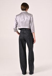 Giacca cropped argentata con maniche a tre quarti abbinata a jeans neri a vita alta con una leggera texture sbiadita e tasche posteriori.