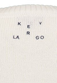 Wit gebreide stof met de tekst "KEY LARGO" in donkerblauwe draden. De tekst is gecentreerd en gestikt op een ribbeltextuur achtergrond.