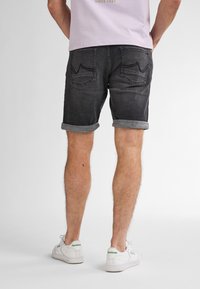 Pantalones cortos de denim negro, con los puños doblados, dos bolsillos traseros con detalles de costura, combinados con zapatillas blancas con acentos verdes.