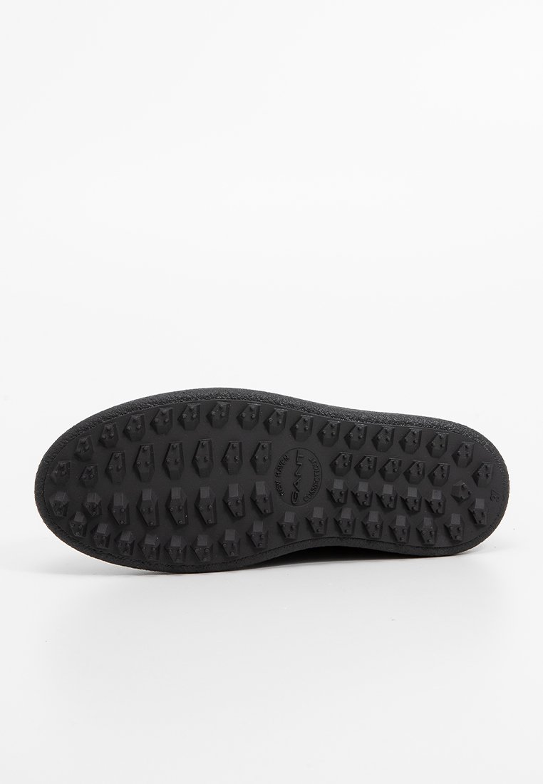 Suela de zapato de goma negra con tacos multidireccionales para mayor agarre, con una superficie texturizada y el logotipo de la marca grabado en el centro.