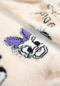 Calze morbide e pelose di colore rosa con un volto di un personaggio dei cartoni animati in bianco e nero, con un accento viola sulla parte superiore, che mostrano un materiale testurizzato e soffice.