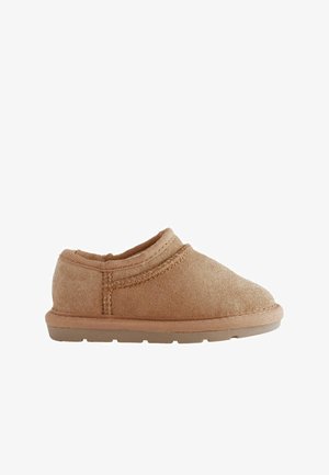 Beige Slipschuhe aus weichem Stoff mit runder Zehenpartie und strukturierter Oberfläche. Eine niedrige Gummisohle und gestickte Akzente sind sichtbar.