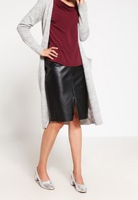 Long gray cardigan, maroon top, and black faux leather skirt with a front slit. Silver heeled shoes complete the look.
