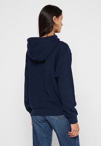 Felpa blu navy realizzata in tessuto morbido, con un grande cappuccio e polsini a costine, dal taglio morbido e senza loghi o motivi visibili.