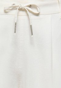 Gros plan sur un pantalon en tissu blanc avec un cordon de serrage noué et des embouts métalliques sur la ceinture.