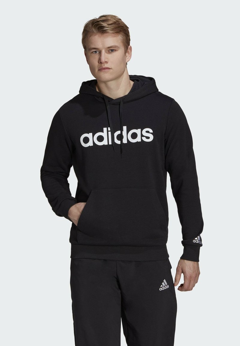 Felpa nera con cappuccio in tessuto morbido, presenta un grande logo bianco "adidas" sul fronte, cappuccio regolabile con coulisse e tasca a marsupio davanti.
