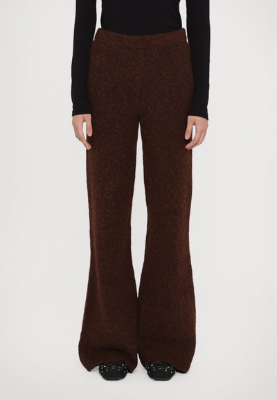 Pantalons marron évasés en tricot avec une finition douce et texturée et une taille élastique. Associés à des chaussures noires avec des accents en argent.